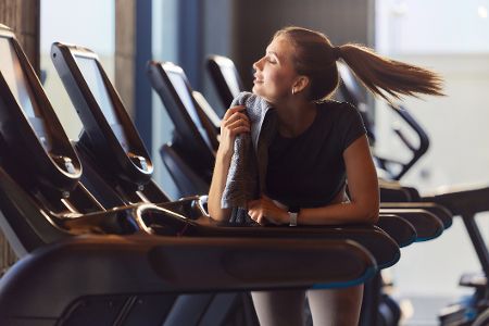 Frau lehnt im Fitnessstudio auf einem Laufband