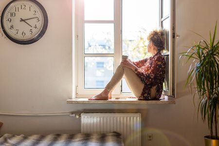 Einsame Frau sitzt auf einer Fensterbank und schaut nach draußen