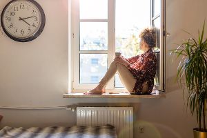 Einsame Frau sitzt auf einer Fensterbank und schaut nach draußen