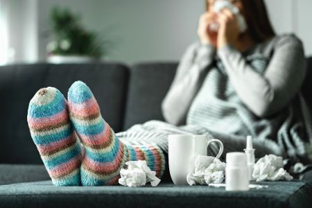 Erkältete Frau mit Wollsocken sitzt auf dem Sofa und putzt sich die Nase