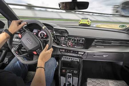 Die Innenraumaufnahme zeigt das Cockpit des Audi RS3 Competition Limited aus der Fahrerperspektive. Sichtbar sind RS‑Sportlenkrad, digitales Kombiinstrument, zentraler Touchscreen und RS‑spezifische Bedienelemente in der Mittelkonsole. Durch die Frontscheibe ist eine Fahrszene auf der Rennstrecke in Hockenheim zu erkennen.
