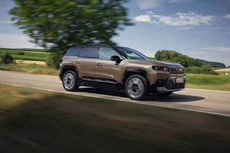Das Foto zeigt einen Jeep Compass Elektro in Fahrt auf einer Landstraße. Der kompakte SUV mit Elektroantrieb ist in klarer Seitenansicht aufgenommen; die Mitzieher-Aufnahme erzeugt Bewegungsunschärfe im Hintergrund.