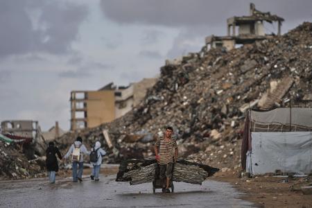Palästinenser trägt Bleche durch Kriegsschutt in Gaza