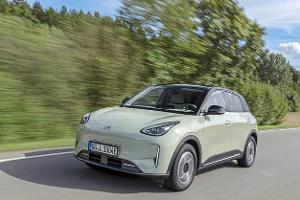 Das Foto zeigt den Geely E2 Ultra in der Karosseriefarbe Polarlichtgrün in Fahrt auf einer Landstraße. Der kompakte Elektro-Crossover mit fünf Türen ist in Dreiviertel-Frontansicht zu sehen, mit schwarzem Kontrastdach und glatter, weitgehend geschlossener Front, wie sie bei Elektroautos typisch ist. Der Kontext entspricht einer Straßenaufnahme im ländlichen Umfeld.