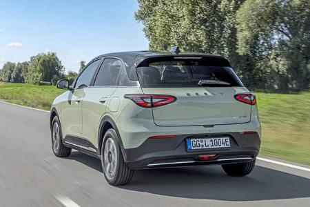 Der Geely e2 Ultra in der Farbe Polarlichtgrün ist in einer dynamischen Fahraufnahme aus schräger Heckperspektive auf einer Landstraße zu sehen. Der kompakte Elektro-Crossover zeigt LED‑Rückleuchten, ein schwarzes Kontrastdach und aerodynamisch gestaltete Räder; am Heck ist der GEELY‑Schriftzug sowie ein deutsches E‑Kennzeichen erkennbar. Die Szene spielt bei Tageslicht in ländlicher Umgebung.