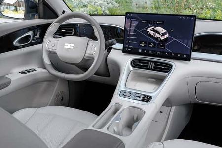 Das Foto zeigt das Cockpit des Geely E2 Ultra in der Ausführung Polarlichtgrün. Sichtbar sind ein großes freistehendes Infotainment‑Display, ein digitales Kombiinstrument, zentrale Luftausströmer sowie eine aufgeräumte Mittelkonsole mit Ablagefach und Cupholdern in hellem Interieur. Die Aufnahme fokussiert die Armaturen und Bedienelemente des vorderen Innenraums.