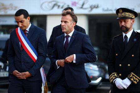 Der französische Präsident Emmanuel Macron (M) besucht nach einer mutmaßlich rassistischen Tat den Ort Trappes.