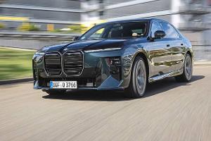 Das Foto zeigt einen BMW 740 xDrive als Limousine in Fahrt auf einer Straße. Die Front mit großer Doppelniere, geteilten Scheinwerfern und aerodynamisch gezeichneten Flächen ist aus schräger Perspektive sichtbar; das Modell verfügt über den Allradantrieb xDrive. Der Hintergrund mit Gebäuden und Bewegungsunschärfe deutet auf eine städtische Umgebung hin (IPTC: Stadt).
