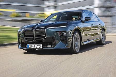 Das Foto zeigt einen BMW 740 xDrive als Limousine in Fahrt auf einer Straße. Die Front mit großer Doppelniere, geteilten Scheinwerfern und aerodynamisch gezeichneten Flächen ist aus schräger Perspektive sichtbar; das Modell verfügt über den Allradantrieb xDrive. Der Hintergrund mit Gebäuden und Bewegungsunschärfe deutet auf eine städtische Umgebung hin (IPTC: Stadt).