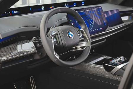 Das Foto zeigt den Innenraum der BMW 740 xDrive mit modernem Cockpit, BMW‑Lenkrad und durchgehendem Curved-Display über dem Armaturenbrett. Sichtbar sind ein volldigitales Anzeigeensemble, ein großes Touchscreen-Infotainmentsystem sowie Carbon-Zierleisten und eine hochwertige Mittelkonsole; die xDrive-Bezeichnung kennzeichnet die Allradvariante der 7er-Limousine.