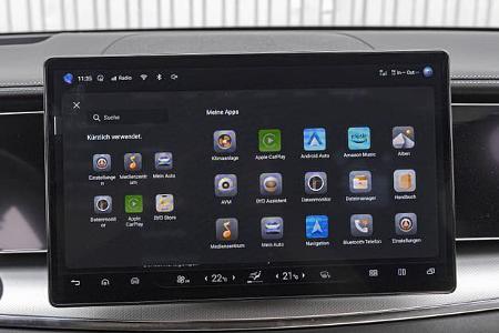 Das Foto zeigt das zentrale Infotainment-Display des BYD Sealion 7 EXcellence AWD. Auf dem Bildschirm ist der App-Launcher mit Funktionen wie Klimaanlage, Apple CarPlay, Android Auto, Navigation und Medienzentrum zu sehen; die Klimabedienung ist als Touchleiste am unteren Rand integriert. Die Aufnahme aus dem Cockpit dokumentiert die Bedienoberfläche und Konnektivitätsfunktionen des Fahrzeugs.