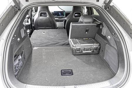 Das Foto zeigt den Kofferraum des BYD Sealion 7 EXcellence AWD mit geöffneter Heckklappe. Die Rücksitzlehnen sind teilweise umgeklappt und vergrößern die ebene Ladefläche; rechts liegt ein Hartschalenkoffer, zudem sind Verzurrösen, Seitentaschen und ein Lautsprechergitter sichtbar. Durch den Innenraum ist das zentrale Infotainment-Display und die Vordersitze zu erkennen.