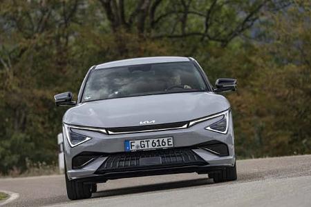 Das Foto zeigt den Kia EV6 GT AWD in Frontalansicht mit der charakteristischen LED-Lichtsignatur und neuem Kia-Logo. Der vollelektrische Allrad-Crossover befindet sich in Kurvenfahrt auf einer Landstraße; die sportlich gezeichnete Frontschürze und aerodynamischen Elemente sind gut erkennbar.