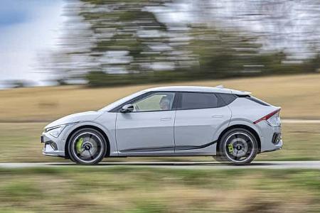 Das Foto zeigt einen Kia EV6 GT AWD in vollständiger Seitenansicht während der Fahrt. Die dynamische Mitzieher-Aufnahme betont die großen Räder mit neongrünen Bremssätteln, die sportliche Crossover-Silhouette und den Allradantrieb der GT-Variante. Der verwischte Hintergrund deutet auf eine schnelle Straßenfahrt in ländlicher Umgebung hin.