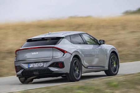 Das Bild zeigt einen Kia EV6 GT AWD in Heck‑Dreiviertelansicht auf einer Landstraße. Die GT-Allradvariante des vollelektrischen Crossover ist in grauer Lackierung mit durchgehendem LED-Leuchtenband, großen Rädern und markanten Aerodynamikelementen zu sehen. Die Aufnahme entstand in Fahrt und zeigt leichte Bewegungsunschärfe im Umfeld.
