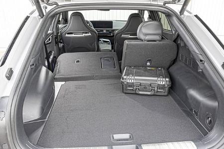 Der Laderaum des Kia EV6 GT AWD ist aus der geöffneten Heckklappe aufgenommen und zeigt eine teilweise umgeklappte Rücksitzlehne, wodurch eine nahezu ebene Ladefläche entsteht. Rechts liegt eine robuste Transportbox, die Größenverhältnis und Nutzbarkeit des Kofferraums veranschaulicht. Als vollelektrisches AWD-Performance-Modell der EV6-Baureihe bietet der Innenraum eine variable Gepäckraumgestaltung.