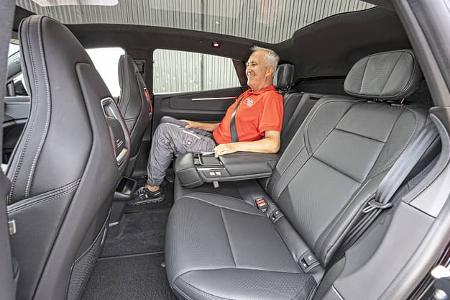 Die Aufnahme zeigt den Fond des Polestar 4 Dual Motor; eine Person sitzt hinten mit heruntergeklappter Mittelarmlehne. Sichtbar sind die schwarz gepolsterten Rücksitze mit ISOFIX-Aufnahmen, Kopfstützen sowie die Rückenlehnen der Vordersitze mit roten Akzenten; die Perspektive betont die Beinfreiheit. Als Dual‑Motor‑Variante handelt es sich um ein vollelektrisches SUV mit Allradantrieb.