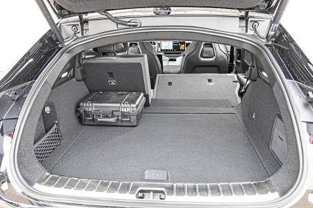 Die Aufnahme zeigt den Gepäckraum des Polestar 4 Dual Motor mit geöffneter Heckklappe; die Rücksitzlehnen sind teilweise umgeklappt und vergrößern den Laderaum. Die ebene Ladefläche reicht bis hinter die Vordersitze, im Hintergrund ist das Cockpit mit großem Zentraldisplay sichtbar.