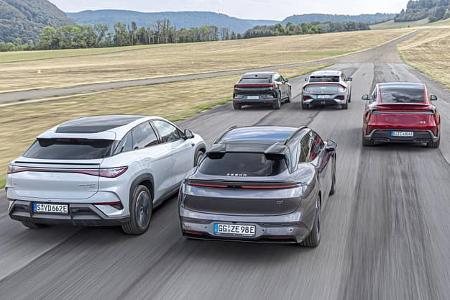 Die Aufnahme zeigt eine Gruppe vollelektrischer Crossover/SUVs im Fahrbetrieb, darunter Kia EV 6 GT AWD, BYD Sealion 7 EXcellence AWD, Polestar 4 Dual Motor, Tesla Model Y Performance und Zeekr 7GT AWD. Alle Modelle verfügen über Elektroantrieb und Allradkonfigurationen; die Szene ist aus der Heckansicht auf einer asphaltierten Fahrbahn in ländlicher Umgebung fotografiert.