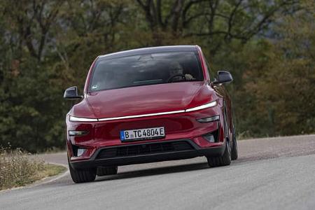 Das Foto zeigt einen Tesla Model Y Performance in roter Lackierung in Frontansicht auf einer Landstraße. Das Elektro-SUV fährt dynamisch durch eine Kurve; die geschlossene Frontpartie und die klaren Linien sind typisch für ein batterieelektrisches Fahrzeug. Die Aufnahme betont die Fahrdynamik und die breite Spur des Crossover-SUV.