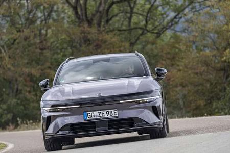 Das Foto zeigt einen Zeekr 7GT AWD in Frontansicht auf einer kurvigen Landstraße. Das Modell mit Allradantrieb wirkt als Elektroauto erkennbar an der geschlossenen Front und dem deutschen Kennzeichen mit „E“, die schmale durchgehende LED-Lichtleiste prägt die Fahrzeugfront. Im Hintergrund stehen herbstlich wirkende Bäume, die Aufnahme vermittelt Fahrdynamik in der Kurve.