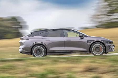 Das Foto zeigt einen Zeekr 7 GT AWD in Seitenansicht während der Fahrt auf einer Landstraße. Der viertürige Fließheckwagen mit Allradantrieb rollt auf großen Leichtmetallrädern; sichtbare rote Bremssättel und ein dunkles Kontrastdach sind erkennbar. Die Aufnahme ist als Mitzieher umgesetzt, wodurch der Hintergrund bewegungsunschärfe zeigt.