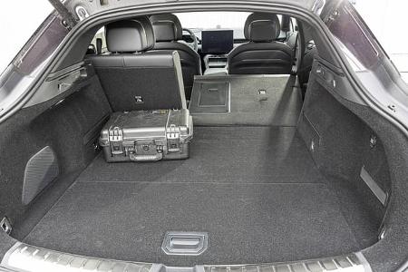 Zu sehen ist der Kofferraum des Zeekr 7 GT AWD mit geöffneter Heckklappe, aus der Perspektive nach vorn in den Innenraum fotografiert. Die geteilte Rücksitzlehne ist teilweise umgeklappt und bildet eine verlängerte, nahezu ebene Ladefläche; ein Hartschalenkoffer dient als Größenreferenz und es sind Verzurrpunkte sowie seitliche Ablagen erkennbar.