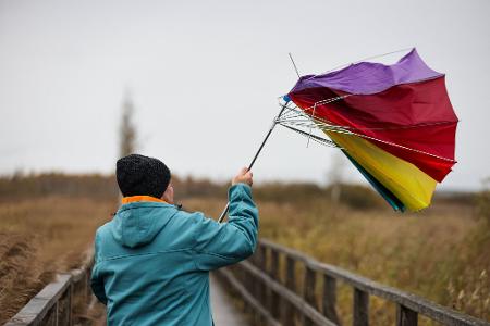 Ein Mann hält auf dem Steg am Federsee seinen Regenschirm fest, der von einer Sturmböe erfasst wird.
